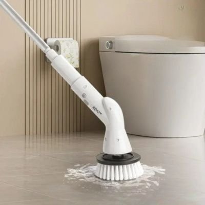 Brosse de nettoyage électrique REVO 6 en 1 sur sol carrelé, tête ronde lavant le carrelage près des toilettes, eau et mousse autour.