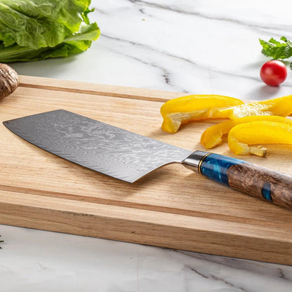 Couteau japonais Nakiri à lame damassée posée sur planche en bois avec poivrons jaunes et légumes en arrière-plan.