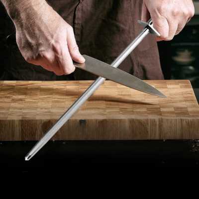affûtage d'un couteau de cuisine avec le fusil à aiguiser, au-dessus d'une planche à découper en bois