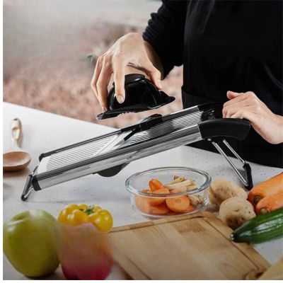 Homme utilisant une mandoline cuisine réglable, tranchant des légumes sur planche avec bol de légumes coupés à côté.
