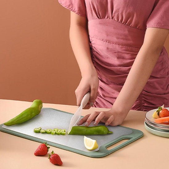 une femme coupe un poivron sur la planche à découper inox, avec deux fraises posées à côté