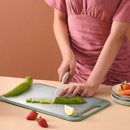une femme coupe un poivron sur la planche à découper inox, avec deux fraises posées à côté