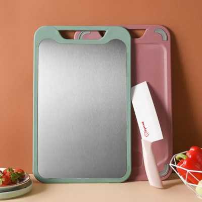 une planche à découper verte et une rose adossées à un mur avecun couteau en céralique blanc, et une coupelle de fraise à côté