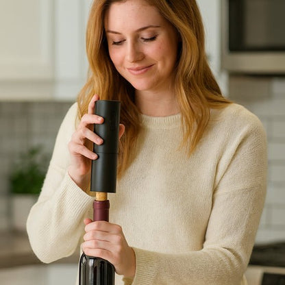 femme blonde souriante débouche une bouteille de vin avec le tire boucon electrique