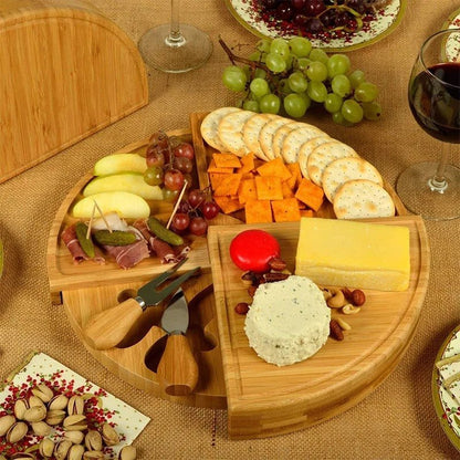 Plateau tournant en bambou avec assortiment fromages, crackers, fruits (raisins, pommes) et charcuterie, garnitures et couverts.