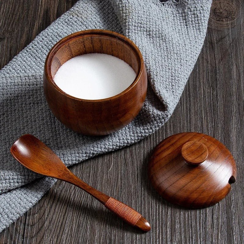 Pot à épices en bois avec son couvercle, rempli de sel, accompagné d'une cuillère en bois sur un linge gris.