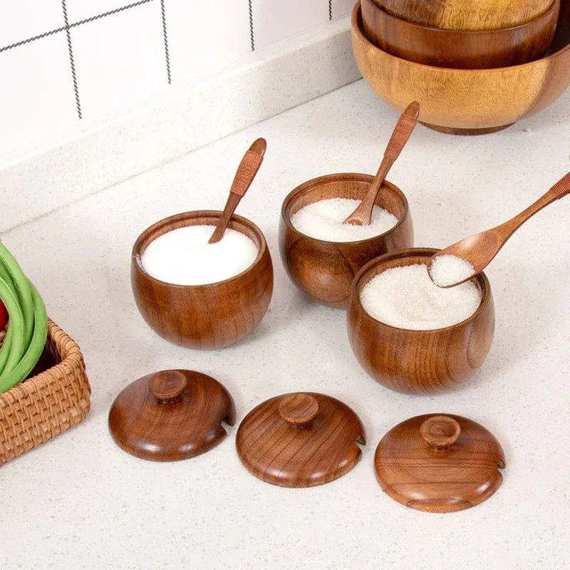 Set de pots à épices en bois avec couvercles, contenants de sucre et lait dans des bols, cuillères assorties sur plan de travail.